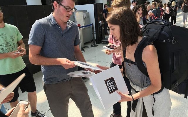 An IfNotNow member distributes materials to a Birthright participant in New York’s JFK airport, Monday, June 18, 2018. (Steven Davidson via Times of Israel)