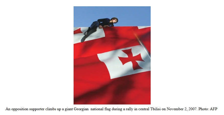 An opposition supporter climbs up a giant Georgian national flag during a rally in central Tbilisi on November 2, 2007. Photo: AFP